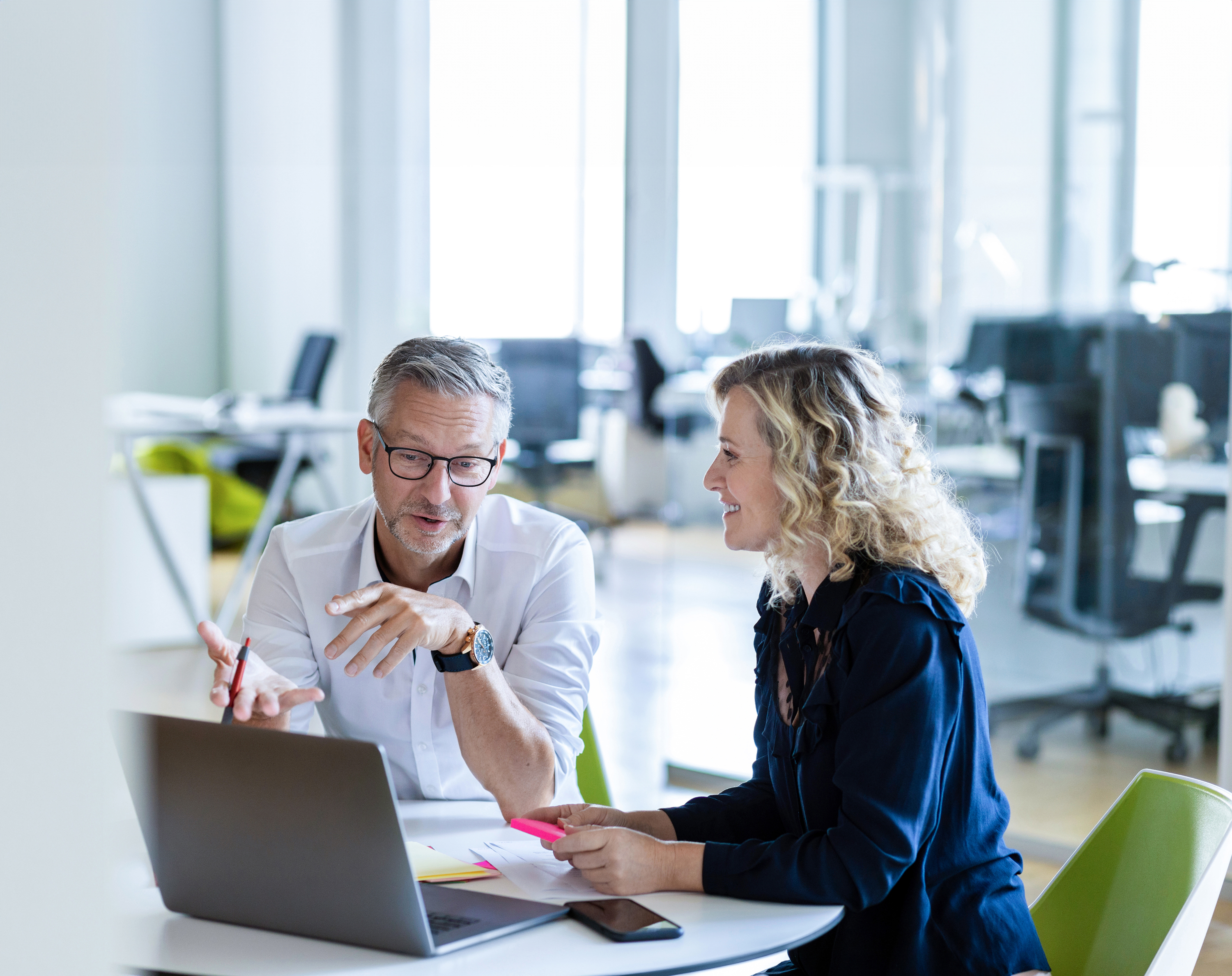 Ein Mann und eine Frau sitzen an einem Schreibtisch über einen Laptop gelehnt und unterhalten sich angeregt