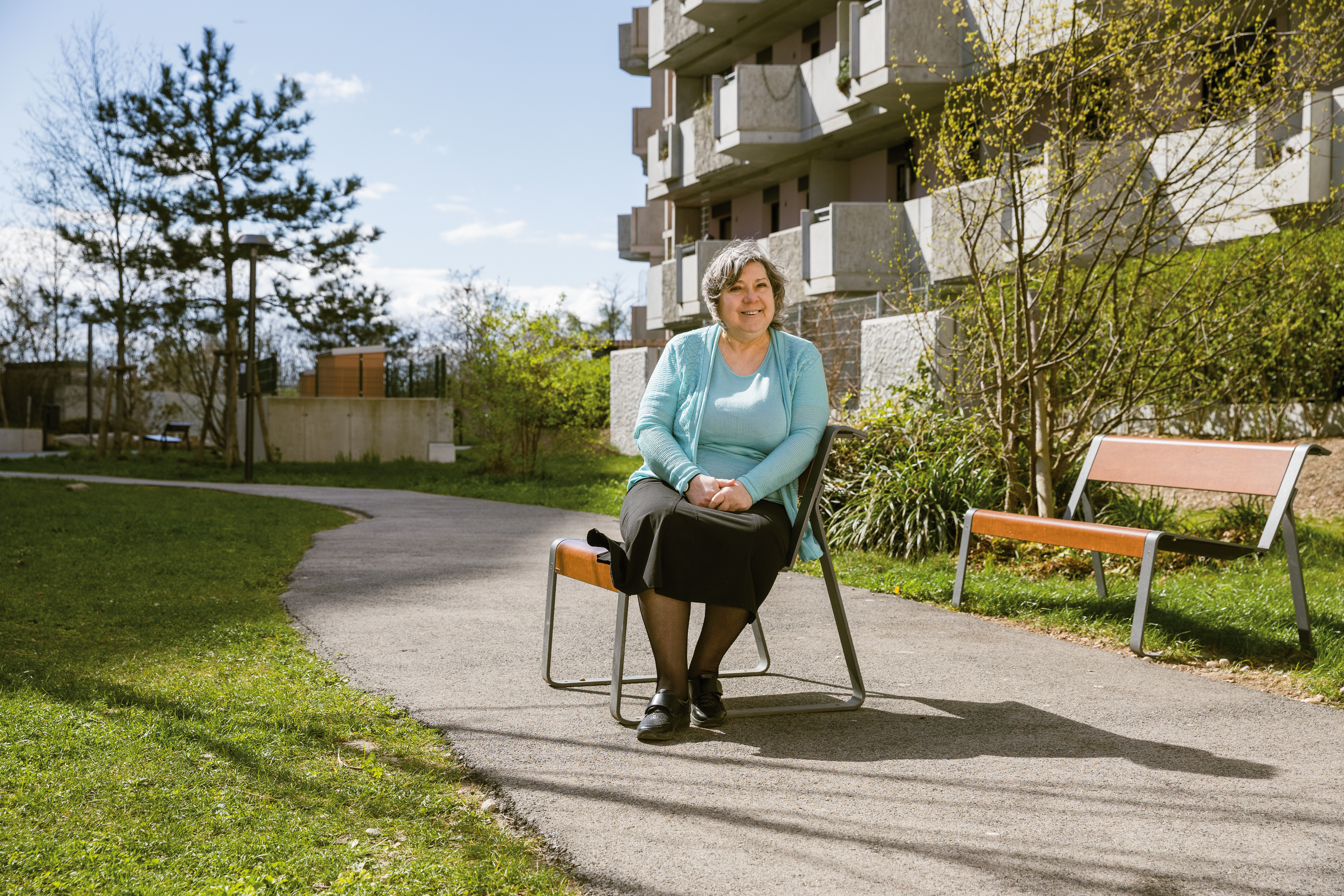Eine ältere Bewohnerin sitzt vor einem ÖSW Haus im Garten und blickt lächelnd in die Kamera